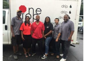 The One Stop Plumbing team members in red, black and gray shirts standing in front of the One Stop Plumbing truck.