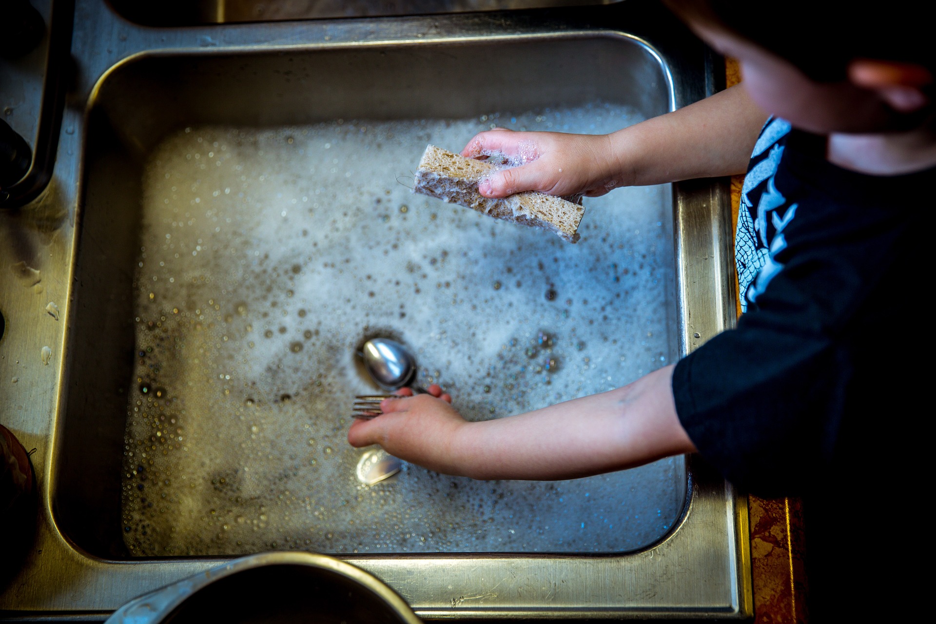 Child standing at the kitchen sink that is full of water and dishes on the One Stop Plumbing drain cleaning page