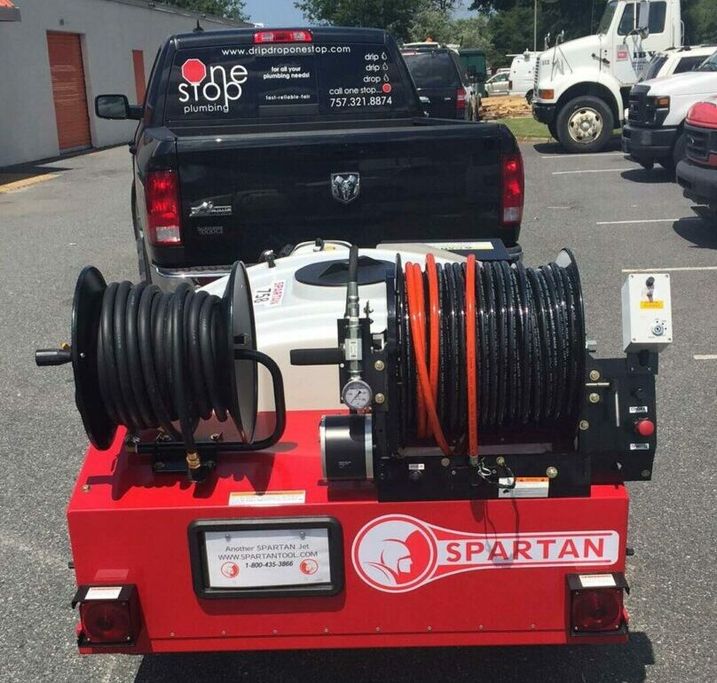 The Spartan Hydro Jetting machine in red towed by the One Stop Plumbing black pickup truck on the One Stop Plumbing Water Jetting page