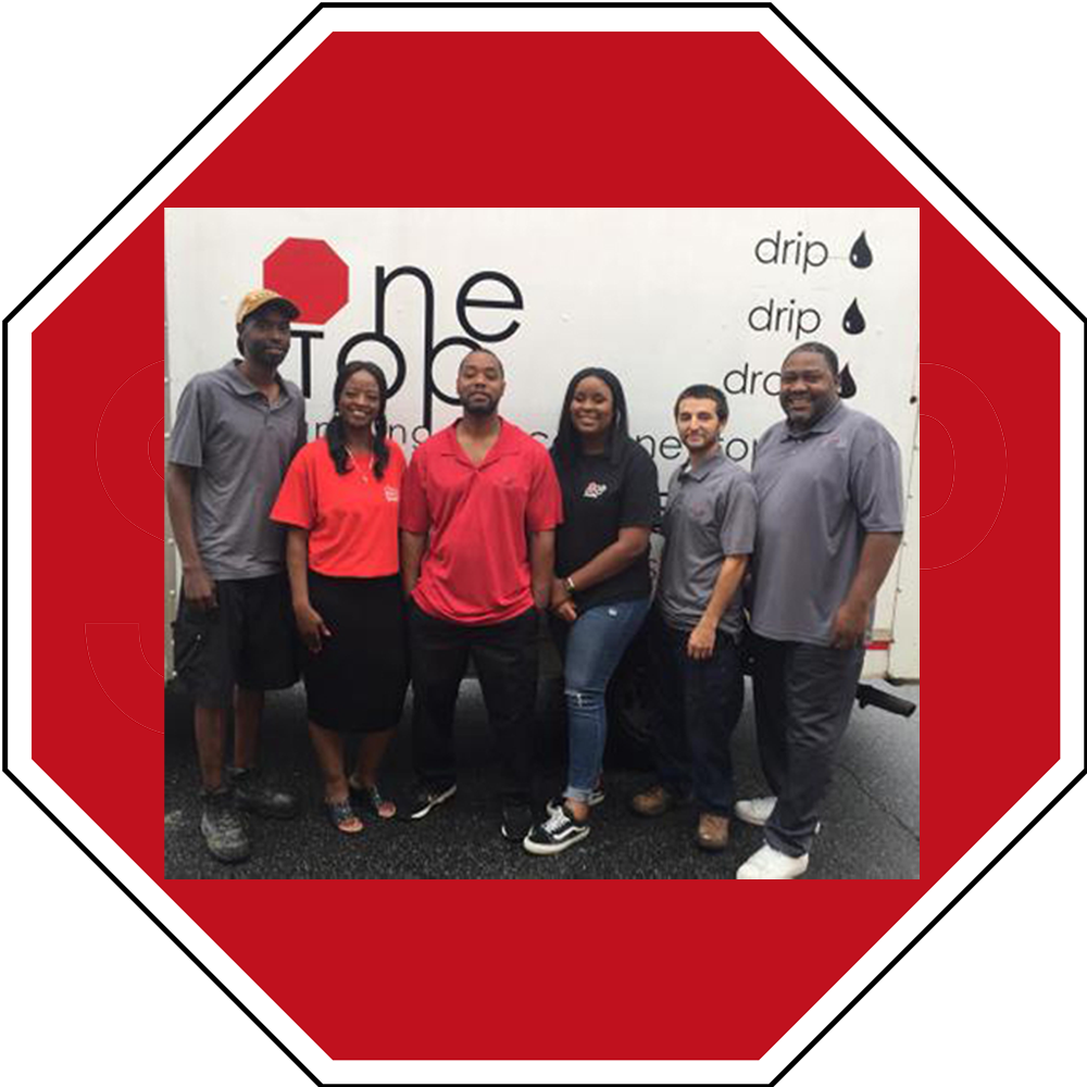 The One Stop Plumbing team members in red, black and gray shirts standing in front of the One Stop Plumbing truck.