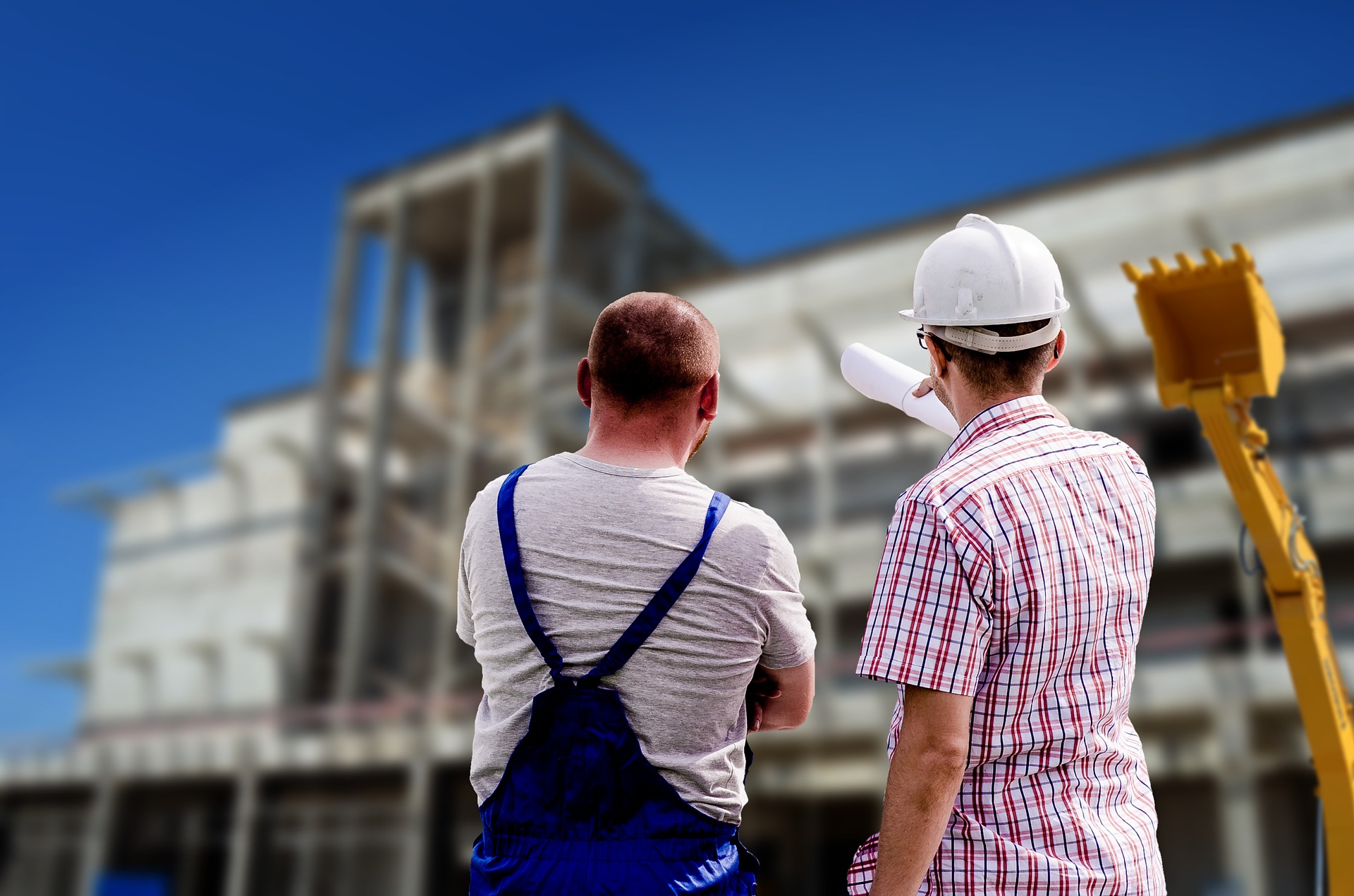 Two construction workers standing outside a new building with a backhoe for plumbing and gas services for builders on the One Stop Plumbing commercial Plumbing page