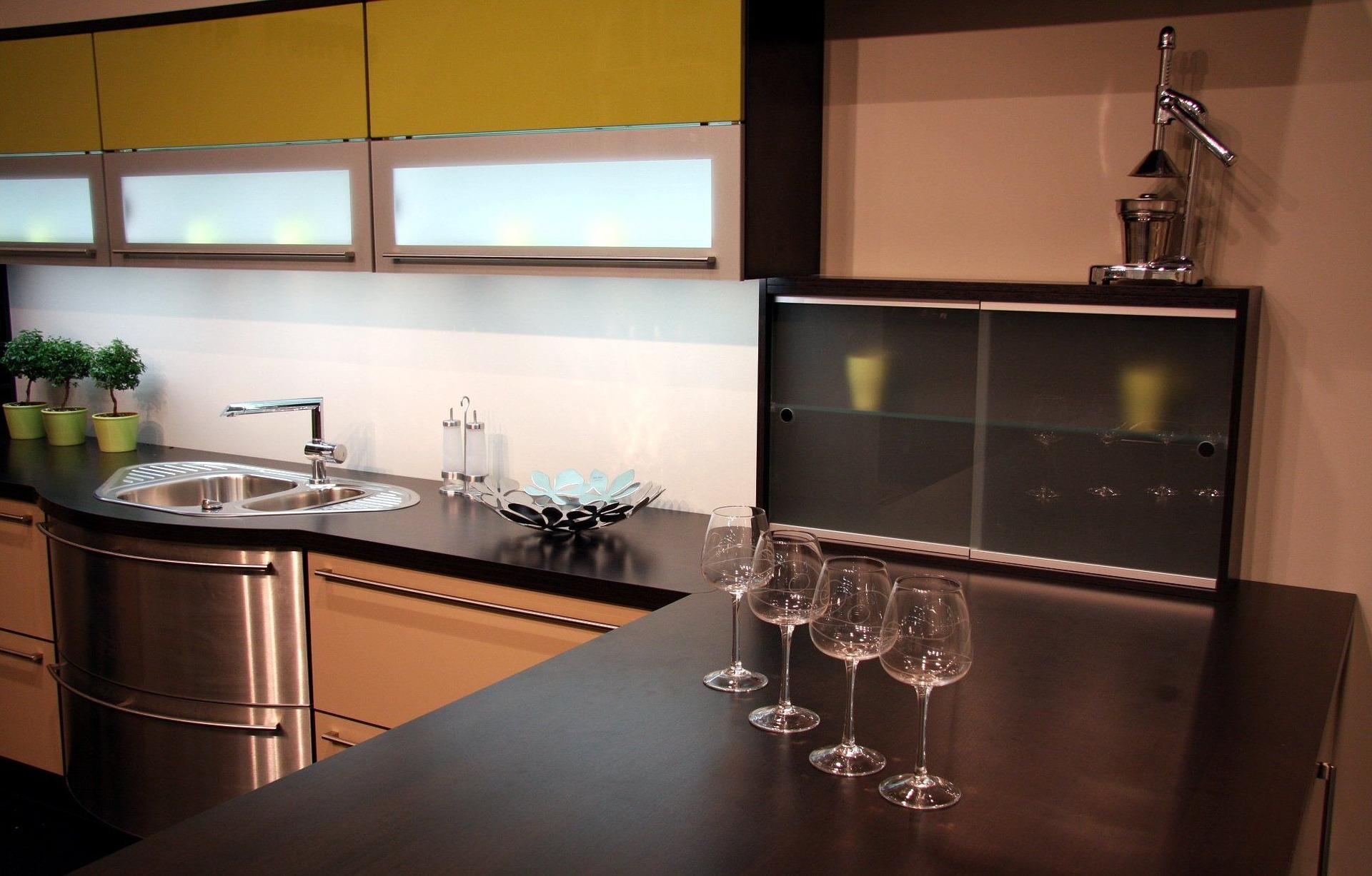 Remodeled wet bar with brown cabinets and black counter tops with wine glasses and a sink on the One Stop Plumbing page for Plumbing Remodeling