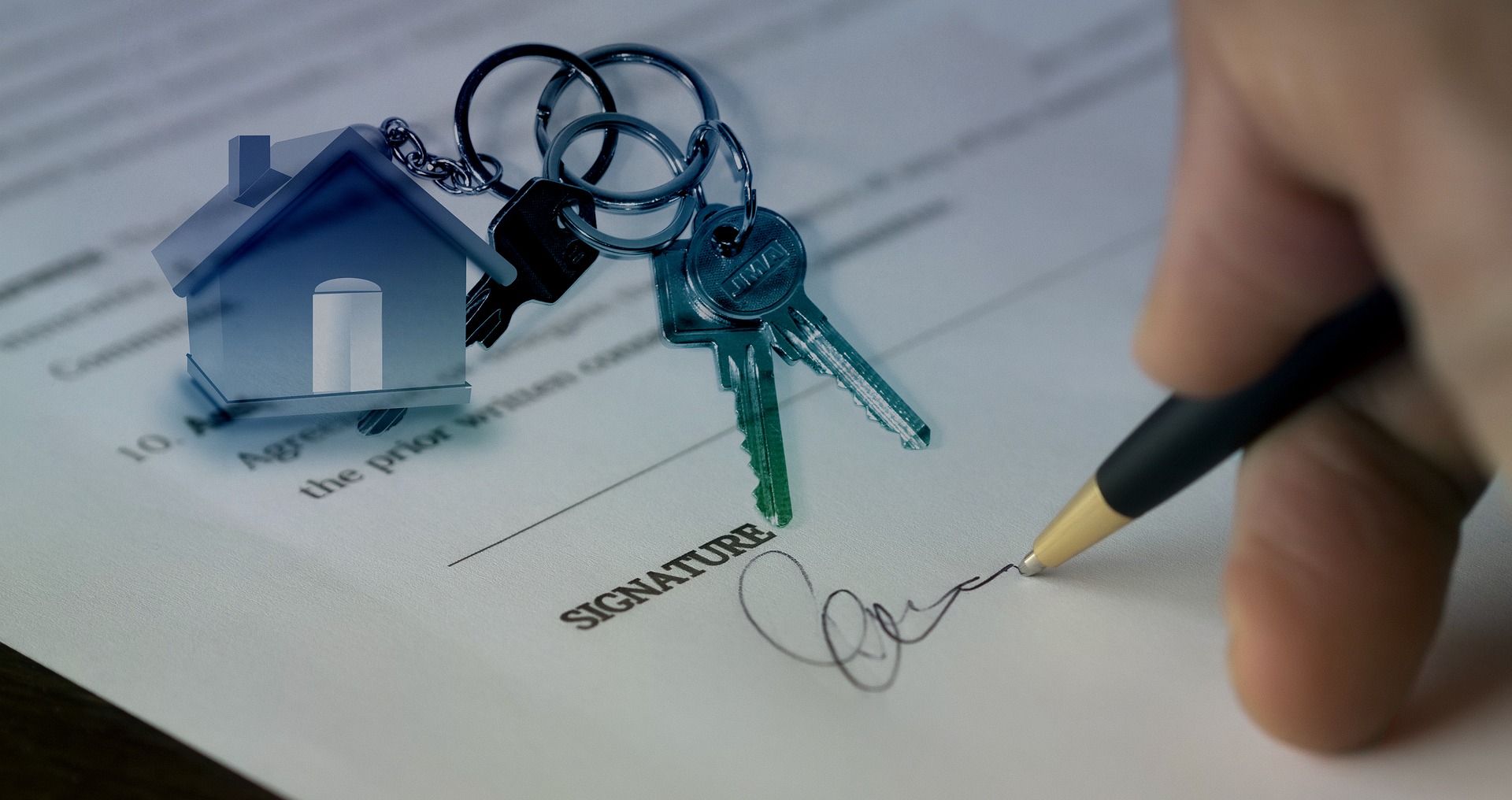 A person signing a document with a set of keys on a house keychain for realtors on the One Stop Plumbing commercial Plumbing page for real estate services