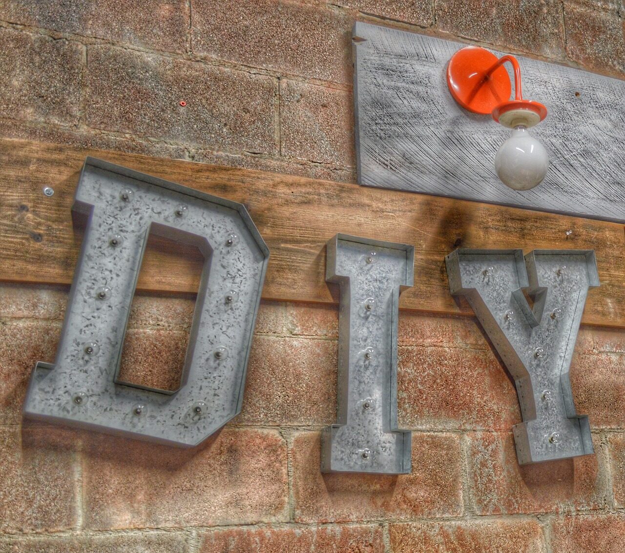 The letters DIY in metal hanging on a brick wall with a red light fixture on the One Stop Plumbing Do It Yourself DIY page