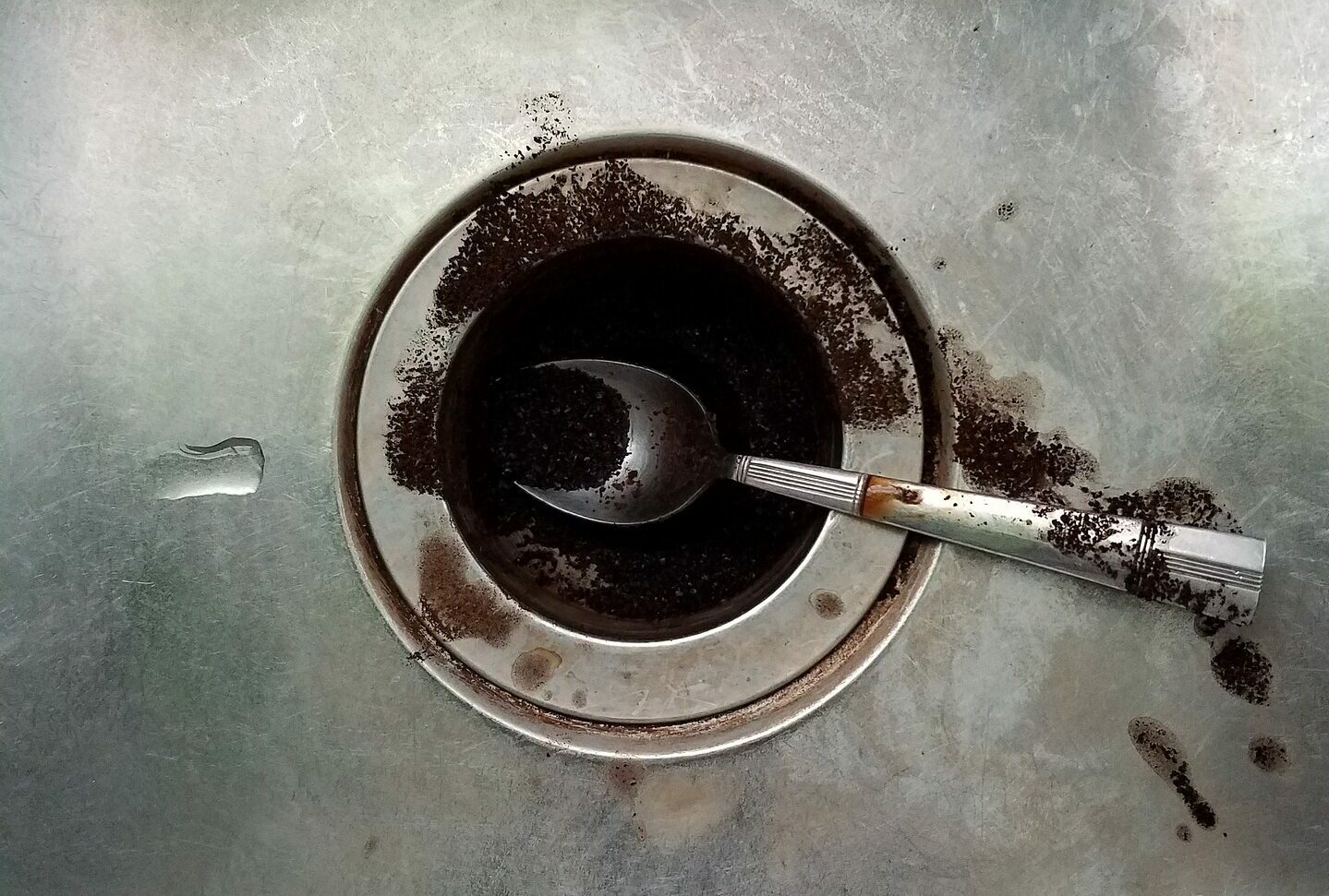 A stainless steel sink drain with a spoon and ground coffee on the One Stop Plumbing garbage disposal page