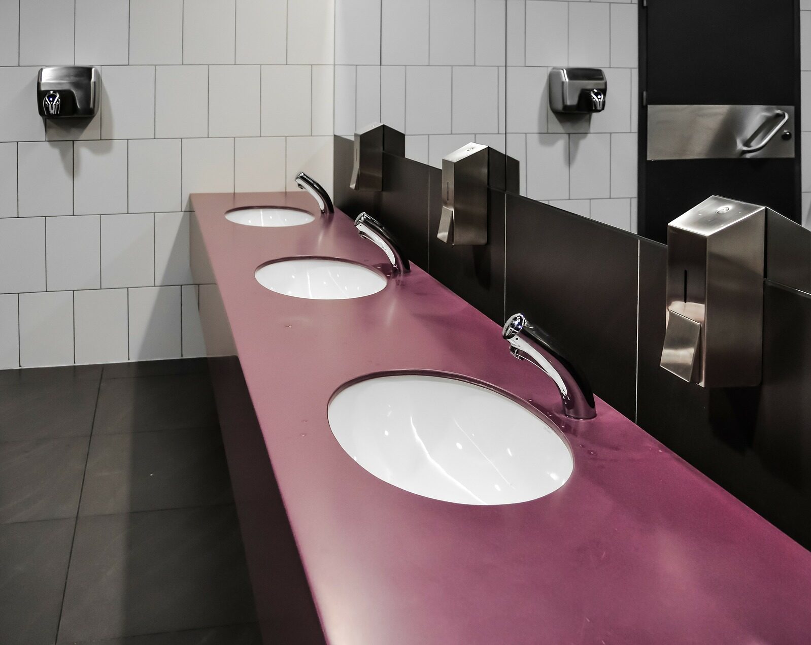 A black, red and white commercial bathroom with 3 sinks, mirror and hand dryer on the One Stop Plumbing commercial Plumbing page