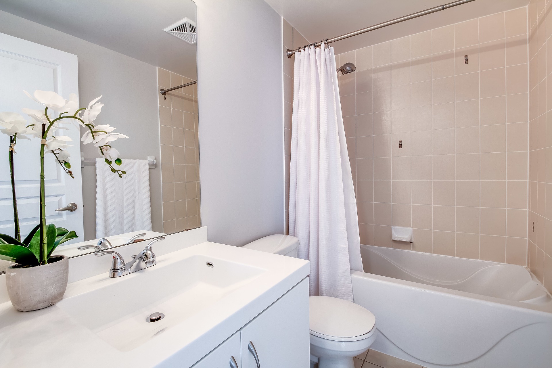 A white bathroom with sink, toilet, faucets and shower tub and brown tile with a flower on the counter on the One Stop Plumbing Faucets, Toilets & Sinks page